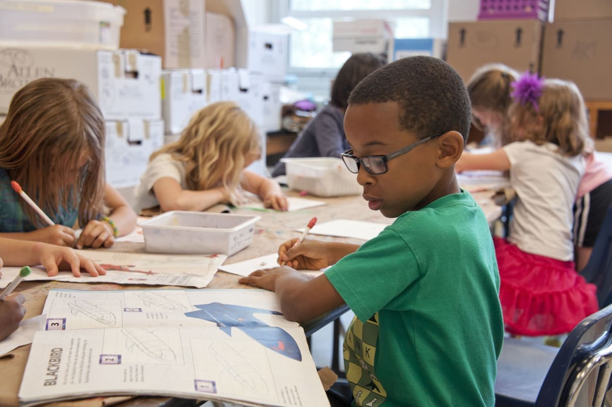 A young student reading and writing at a classroom table