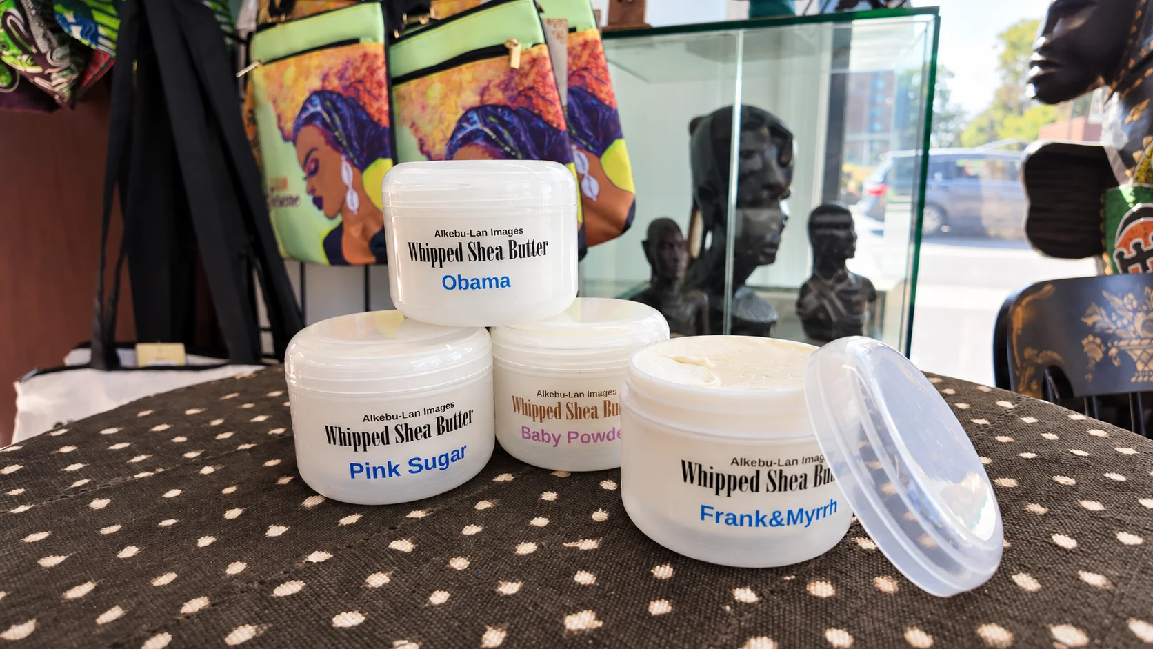 Four jars of Alkebu-Lan Images whipped shea butter on patterned cloth, with one jar open